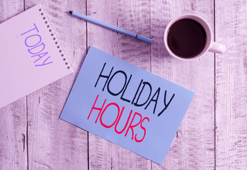 Writing note showing Holiday Hours. Business concept for employee receives twice their normal pay for all hours Stationary placed next to a cup of black coffee above the wooden table