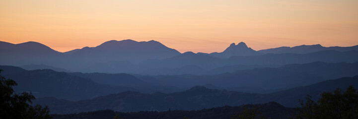 Panoramic silhouette of mountains against an orange sky.