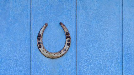 Old iron lucky horseshoe with nails, the ends point up to catch the luck, on a vintage blue wooden door with cracked peeling paint 