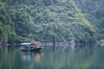 A fisherman in his fishing boat afloat in the emerald green waters near Cat Ba Village in Ha Long Bay, North Vietname