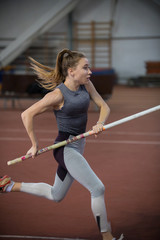 Pole vaulting indoors - young fit woman running with a pole in the hands