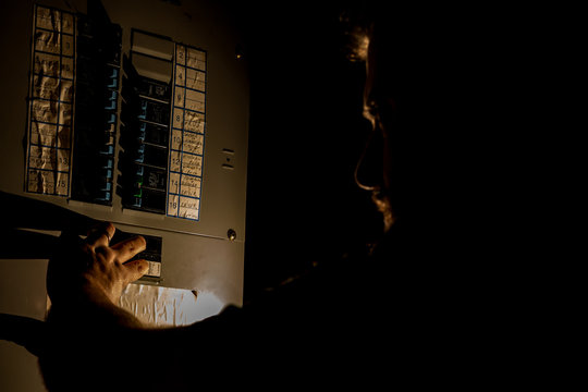 Man Checks Home Fuse Box in a Dark Power Outage