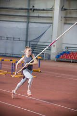 Fototapeta na wymiar Pole vaulting indoors - young woman in leggins running with a pole in the hands