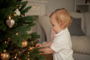 Little cute girl of 2 years in pajamas decorates a Christmas tree. Christmas. New Year. Holidays. Cozy.