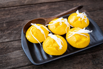 Kanom tan in a black ceramic dish and a wooden spoon placed on a wooden table. Top view.