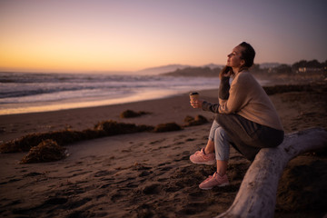 Naklejka premium Woman enjoying hot drink on a sunset near ocean