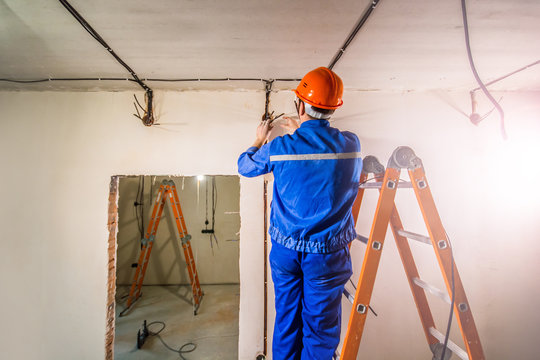 Electrician in hard hat and uniform standing on step ladder