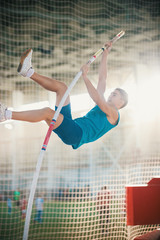 Pole vaulting indoors - young fit man jumping leaning on the pole - sport stadium
