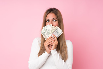 Young blonde woman over isolated pink background taking a lot of money