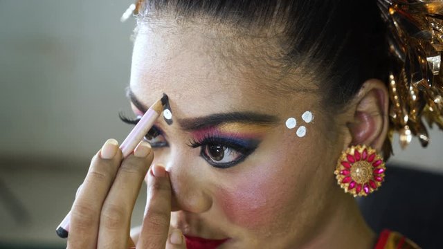 Balinese dancer painting her forehead during applying makeup in the studio. Shot in 4k resolution