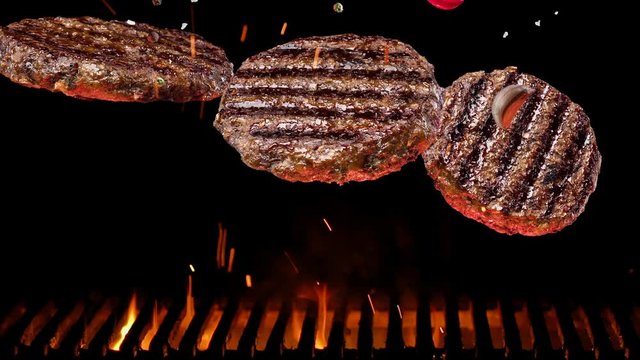 Fried burger patties with spices and salt slowly fall over a barbecue grill, coals burn below.