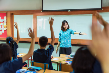 An smiling Asian female high school teacher teaches the blue uniform students in the classroom by...
