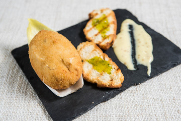 Typical spanish croquette cooked with bread and sauce on slate plate