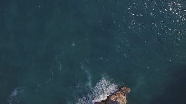 Aerial shot of an old fortress splashed by waves. Next to the fortress is a seafront restaurant and boats in the dock. Petrovac, Montenegro