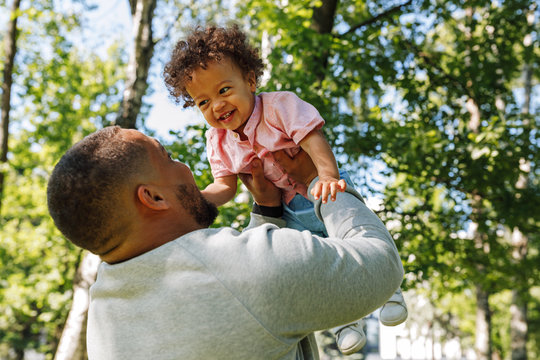 Young dad having fun with toddler son lifting up high outdoors