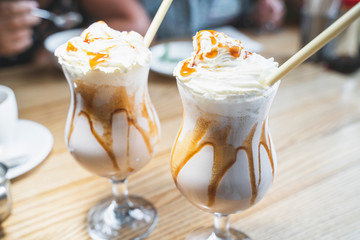 Milk shake with whipped cream and caramel topping in glasses with eco-friendly bamboo straw in cafe. Plastic free concept