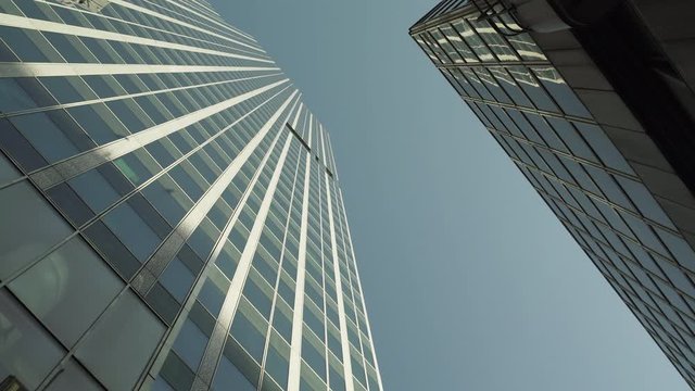 Two Skyscrapers with green glass windows at business district in Paris, looking up low angle barel roll, wide shot with reflections. Futuristic modern building in Blue Sky. 4K UHD. Green black.