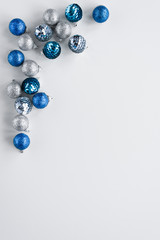 Scattered silver and blue little shiny baubles arranged as a frame on white background. Vertical card with minimalistic christmas theme decoration. Copy space for greetings.