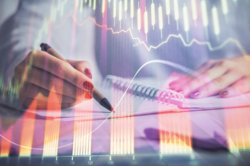 Double exposure of woman's hands making notes with forex graph hologram. Concept stock market analysis.