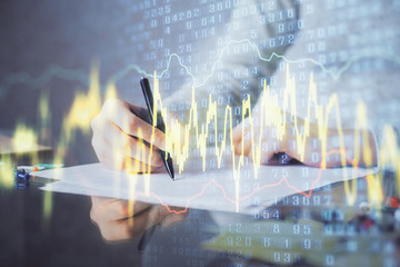 Hand taking notes in notepad. Forex chart holograms in front. Concept of research. Multi exposure