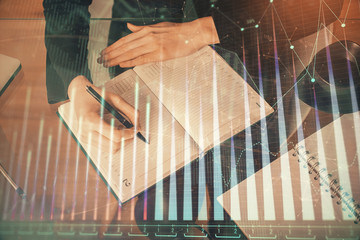 Forex chart hologram on hand taking notes background. Concept of analysis. Multi exposure