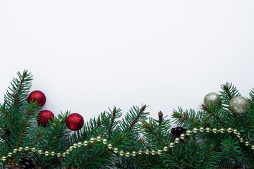 Bottom frame arranged with evergreen christmas tree branches, cones, little red and gold baubles and chain. Winter holidays greeting card with copy space for wishes.