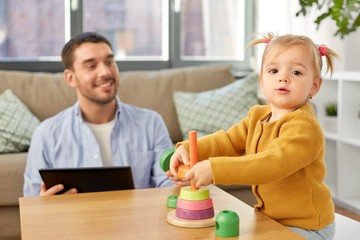 family, fatherhood and people concept - happy father with tablet pc computer and little baby daughter playing with pyramid toy at home