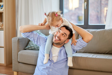 family, parenthood and fatherhood concept - happy father riding little baby daughter on his neck at home