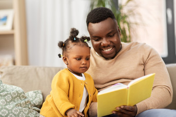 family, fatherhood and people concept - happy african american father reading book for baby...