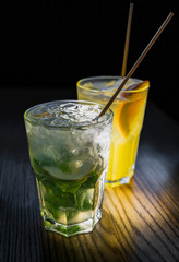 Non-alcoholic mojito in weeping glass with eco-friendly bamboo straw on wooden table in the foreground. Fruit cocktail with orange slice and eco small tube on the background. Plastic free concept