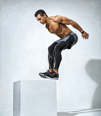 Athletic man doing a box jump exercise routine. Photo of muscular man on grey background. Strength...