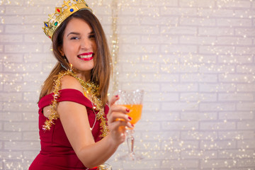 Beautiful woman with a golden crown of king magician and glass of champagne, celebrating the new year.