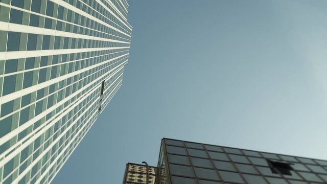 Three Skyscrapers with green glass windows at business district in Paris, looking up low angle barel roll, wide shot with reflections. Futuristic modern building in Blue Sky. 4K UHD. White and green.