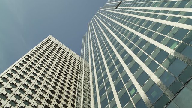 Two Skyscrapers with green glass windows at business district in Paris, looking up low angle tracking in, wide shot with reflections. Futuristic modern building in Blue Sky. 4K UHD. White and green.