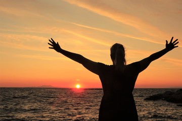 silhouette of a woman with open arms raised at sunset