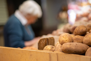 Closeup of potatos at vegetable market, with blurred female customer buying food in background