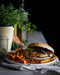 Zucchini and cheese burger accompanied by sweet potato chips. Dark Mood. Food photography.
