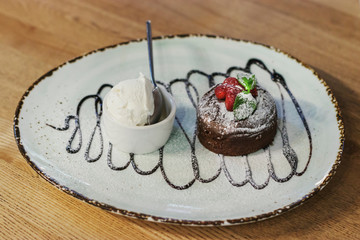 Delicious beautiful dessert on a large plate: brownie with strawberries and a scoop of ice cream with a spoon