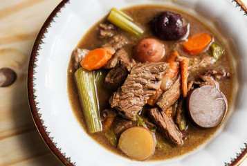 Beef stew in a white bowl with gold rim. Overhead close up view. 