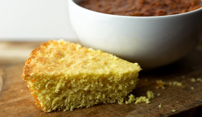 Close up view of a piece of cornbread next to a white bowl filled with red chili.
