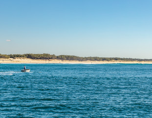 Little dingy floats with a fisherman, just of the shore with surfers waiting for their next wave in the distance