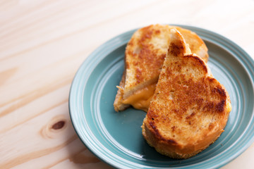 Whole grilled cheese sandwich, cut in half on a blue plate and wooden table. 