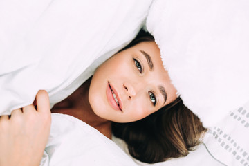 Fototapeta na wymiar A young beautiful woman with long hair wakes up on the white bed at home,