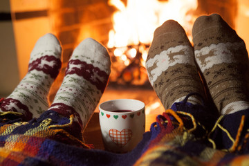 Man and woman in warm knitted socks with cups of hot punch in front of the fireplace