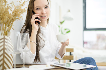 A woman in a white shirt is drinking coffee in a cafe. A female office worker at a lunch break solves a business problem by phone. Mid-level manager