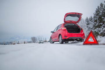 Broken car and warning triangle on the snowy winter road.