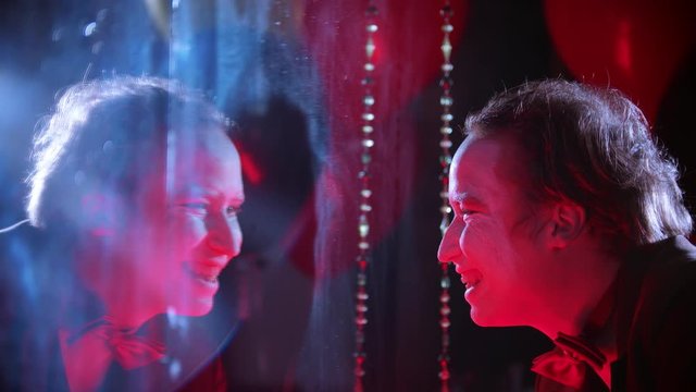A scary man clown with a white paint on his face looking in the mirror and smiling