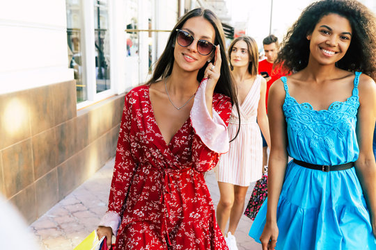 Adorable women. Close up photo of three girls walking along the city streets in beautiful dresses, posing with sunglasses, smiling and looking in the camera.