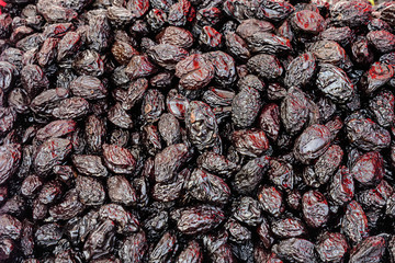 Heap of dried dark blue black organic plums displayed for sale at a street food market, top view or flat lay of tasty healthy food photographed with soft focus