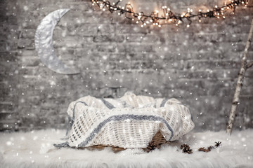 Basket for a newborn baby with a blanket in a Christmas studio interior with a garland, moon and snow 